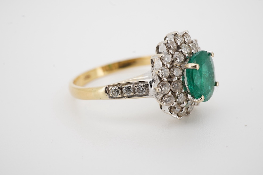 A modern 18ct, emerald and diamond set oval cluster ring with diamond set shoulders, size N/O, gross weight 4.1 grams. Condition - poor to fair